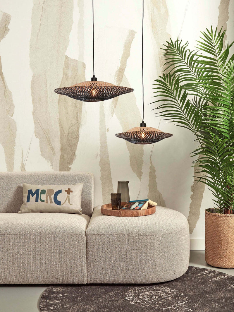 Zwei Hängeleuchten Kalimantan aus Bambus in Schwarz/Natur über einem hellen Sofa mit Palme im Hintergrund.