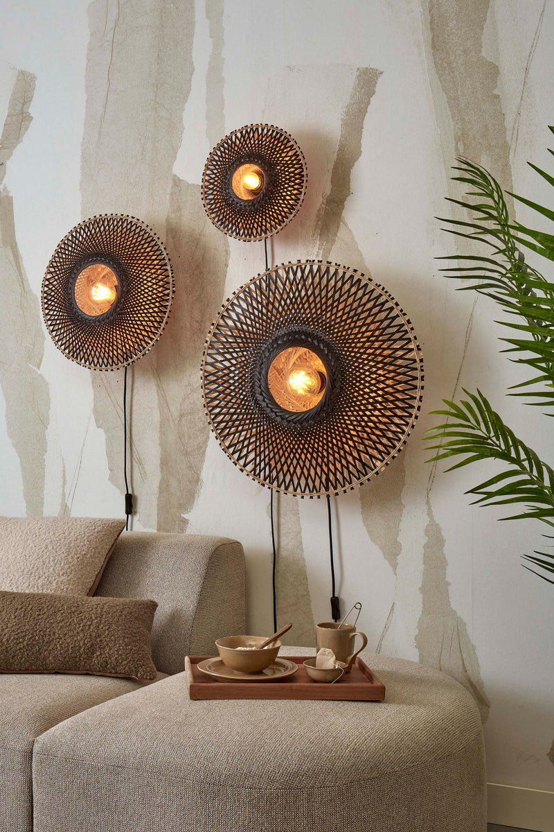 Drei runde Wandleuchten aus geflochtenem Bambus in Schwarz/Natur, von innen beleuchtet, über einem beigen Sofa.