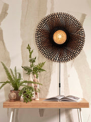 Wandleuchte Kalimantan von Good&Mojo mit geflochtenem Bambusschirm in Schwarz-Natur, an der Wand über einem Holztisch.