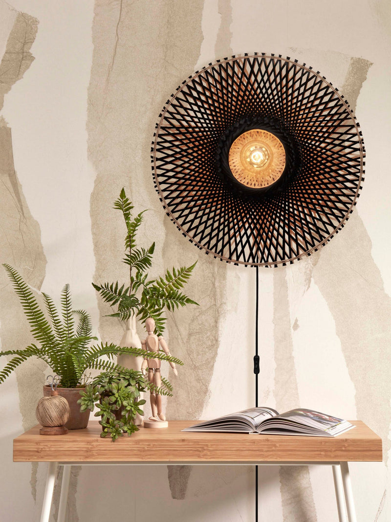 Wandleuchte Kalimantan von Good&Mojo mit geflochtenem Bambusschirm in Schwarz-Natur, an der Wand über einem Holztisch.