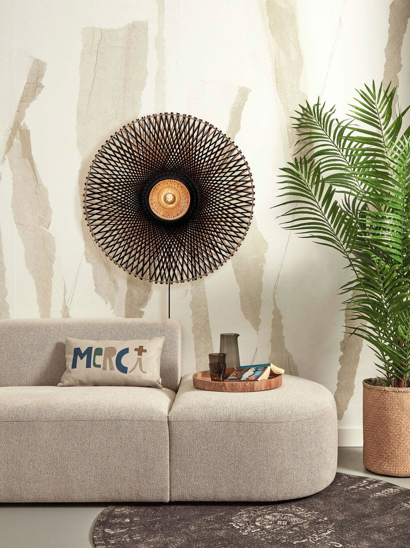 Runde Wandleuchte Kalimantan von Good&Mojo aus geflochtenem Bambus in Schwarz/Natur, an einer Wohnzimmerwand über einem Sofa.