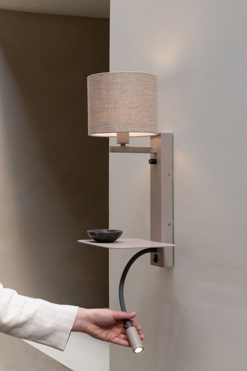 Wandleuchte Florence mit Leinenschirm, flexibler Leselampe und Ablage in Sand, an der Wand montiert, von einer Hand gehalten.