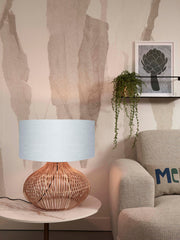 Tischleuchte Kalahari von Good&Mojo mit hellgrauem Leinenschirm und geflochtenem Rattanfuß auf einem Beistelltisch.