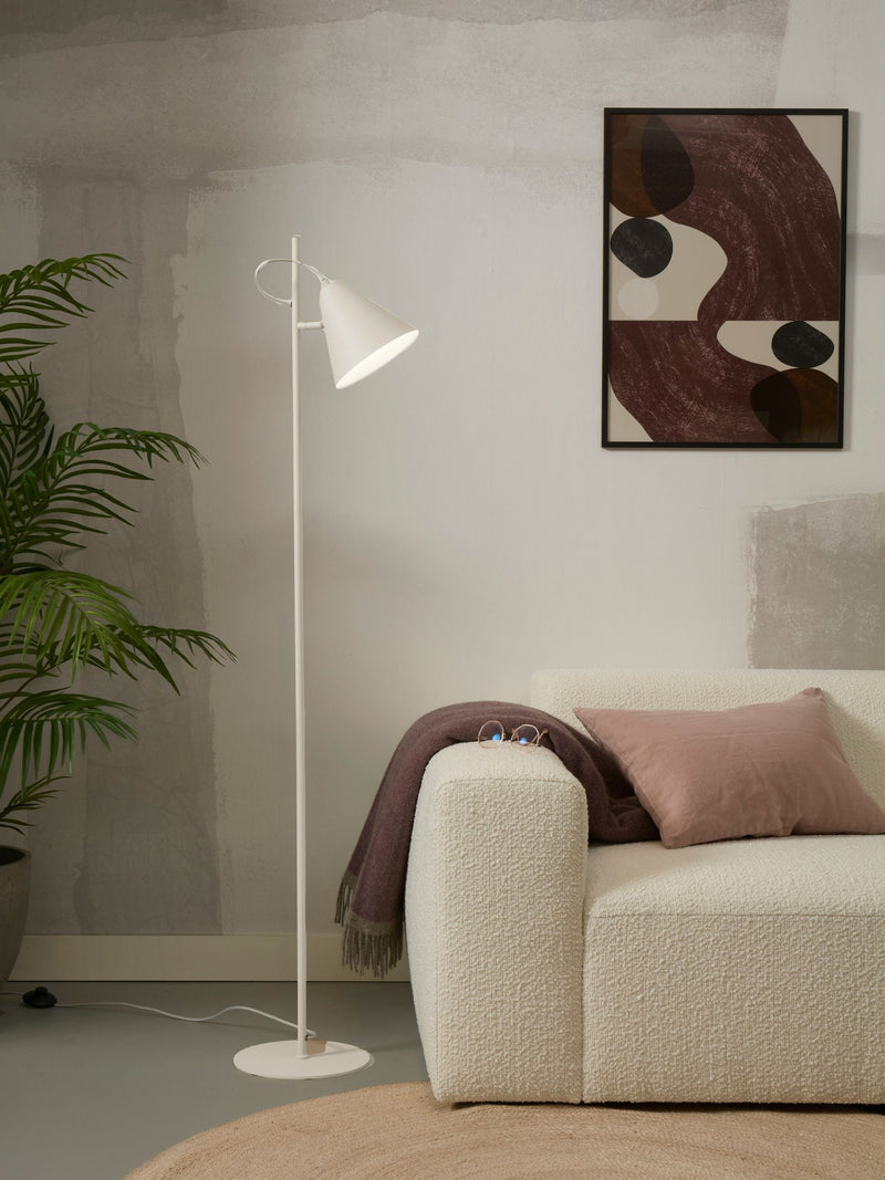 Gesamtansicht der weißen Stehleuchte It's about RoMi Lisbon mit spitzem Eisenschirm neben einem Sofa mit Kissen und Decke.