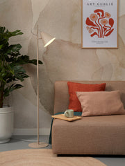 It's about RoMi Stehleuchte Lisbon mit spitzem Schirm in Sand, aufgestellt neben Sofa und Pflanze in warmem Wohnraum.