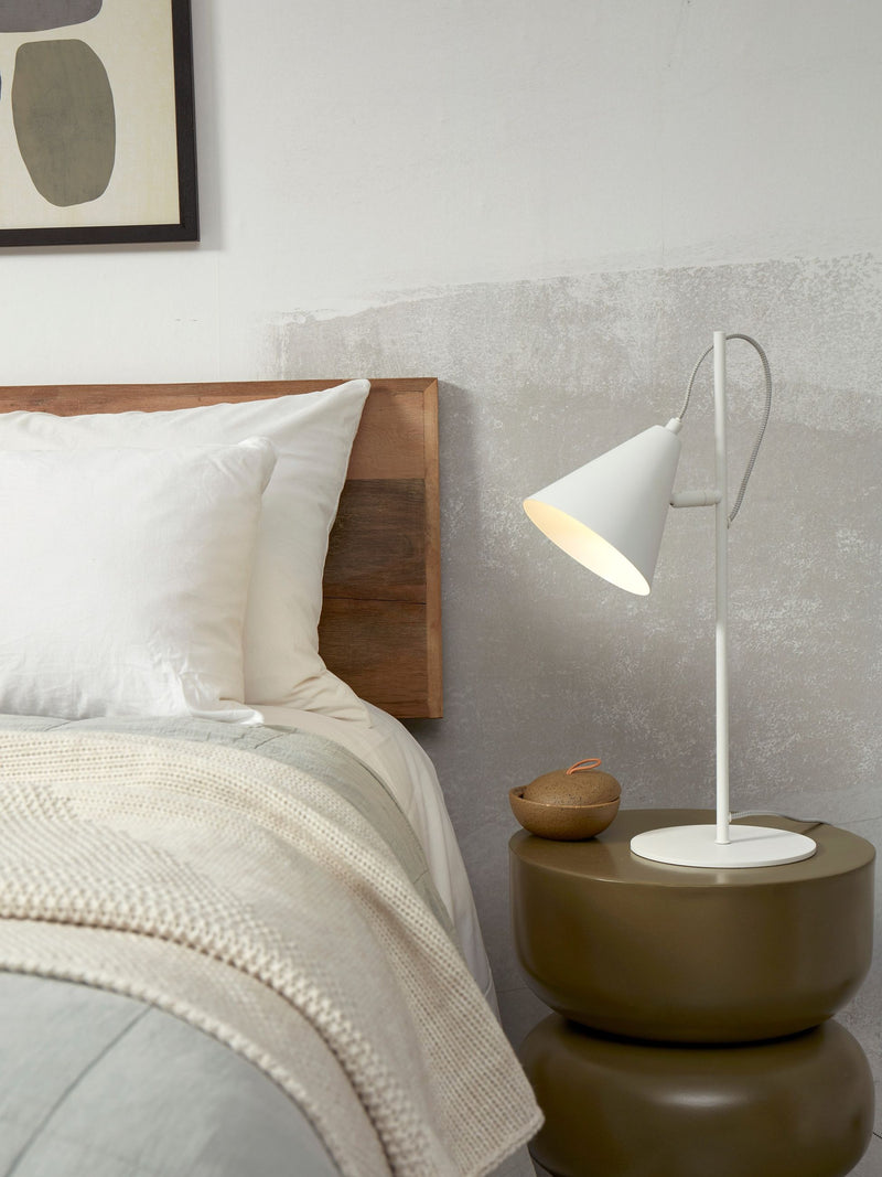 Tischleuchte RoMi Lisbon in Weiß mit kegelförmigem Schirm aus Eisen auf schlankem Gestell neben einem Bett.