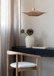 Hängeleuchte Madura von Good&Mojo aus Bambus in Erdtönen über einem Sideboard mit Keramikvase und Blumen.
