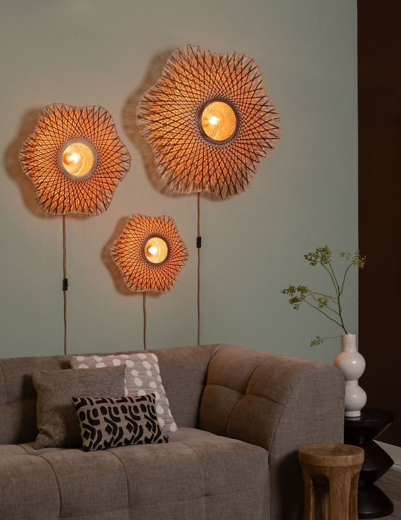 Drei geflochtene Bambus-Wandleuchten Madura in Blütenform, an einer Wand über einem Sofa angebracht und eingeschaltet.