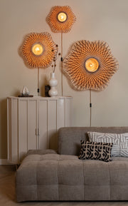 Drei Wandleuchten aus geflochtenem Bambus hängen über einem Sideboard mit Blumenvase und Kissen auf dem Sofa.