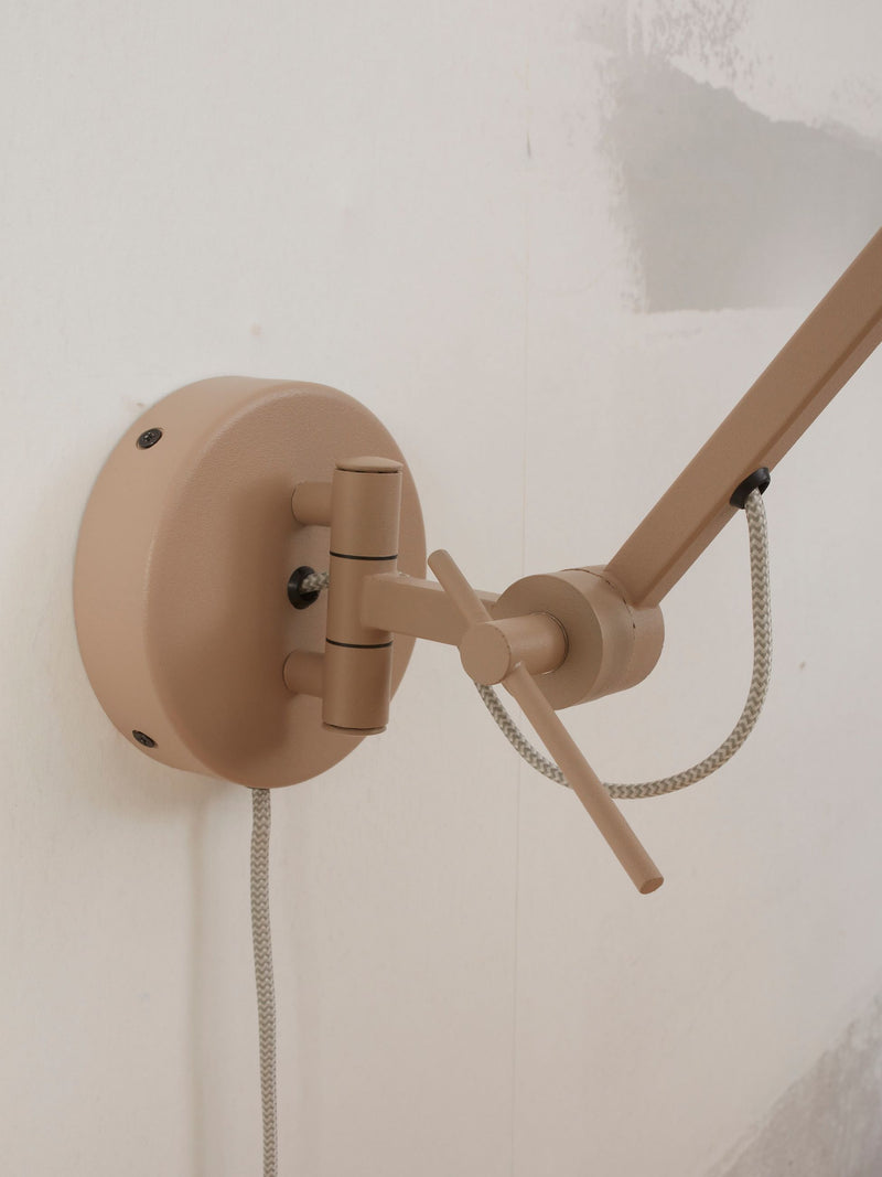 RoMi Wandleuchte Marseille in Sand: Detailansicht des sandfarbenen Eisen-Wandgelenks mit Stoffkabel an weißer Wand.