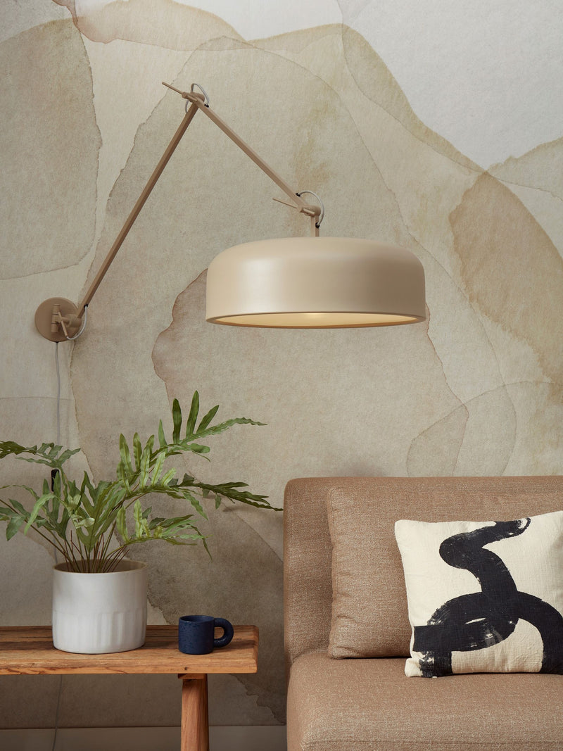 Wandleuchte Marseille in Sand mit ausladendem Gelenkarm und runder Schirmleuchte vor beige gemusterter Wand.