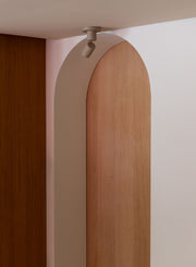 Deckenstrahler It's about RoMi Milan aus Aluminium in Sand, an einer Decke montiert, vor einer Holzbogenwand.