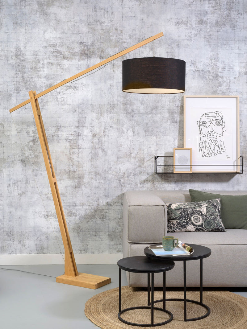 Good&Mojo Stehleuchte Montblanc mit schwarzem Schirm und Bambusgestell, im Wohnzimmer vor grauer Wand neben Sofa.