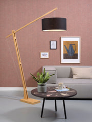 Stehleuchte Montblanc mit hellem Bambusgestell und schwarzem Leinenschirm, im Wohnzimmer vor rosa Wand neben grauem Sofa.
