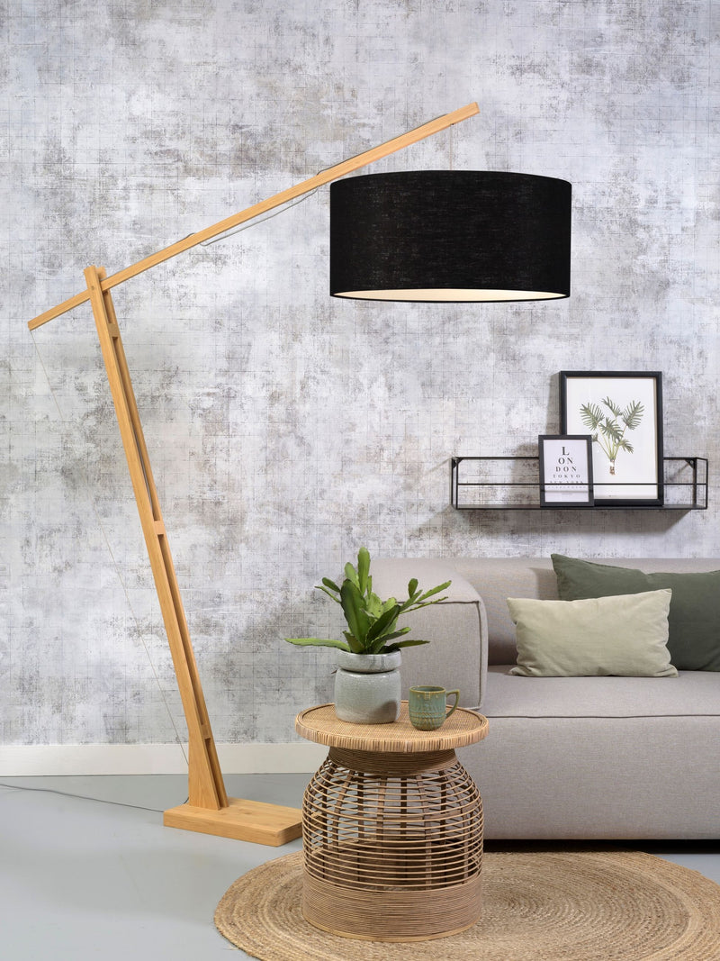 Stehleuchte Montblanc mit schwenkbarem Bambusgestell und schwarzem Leinenschirm, im Wohnraum vor einer Wand neben einem Sofa.