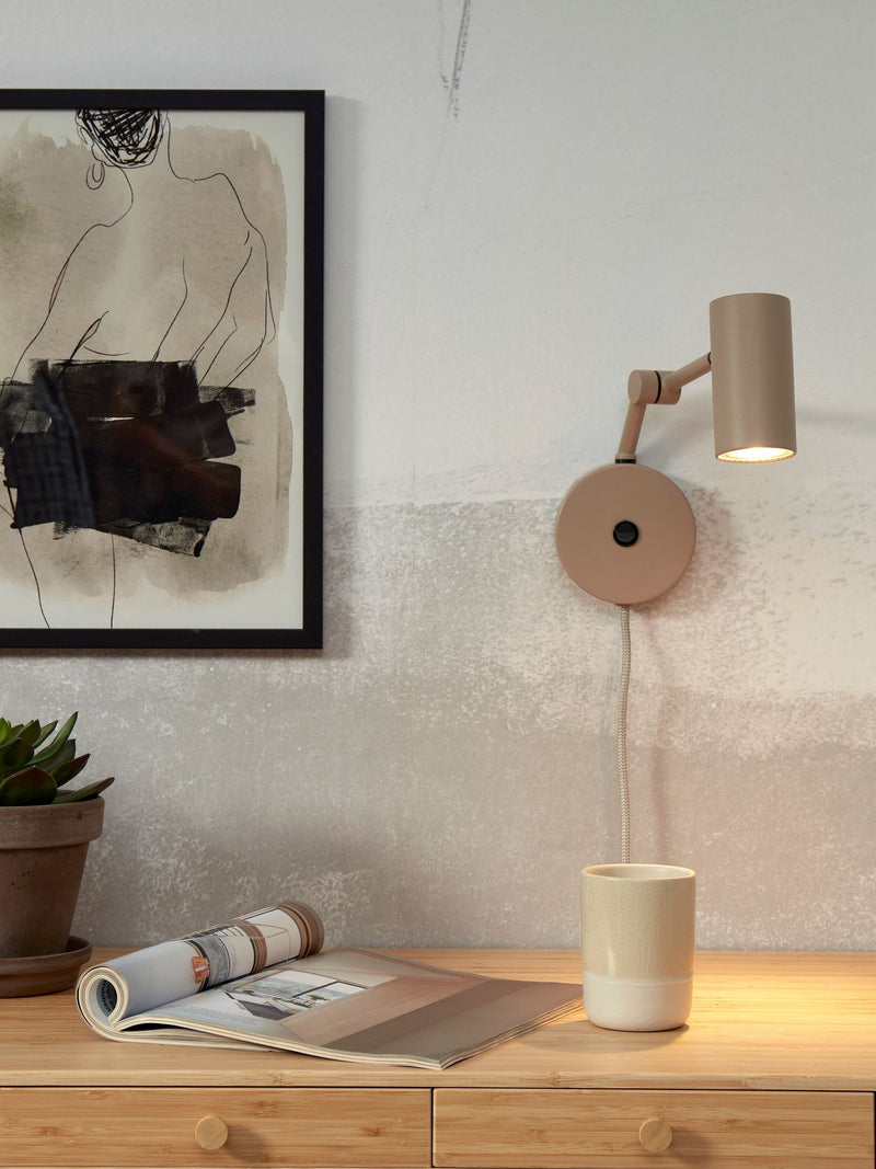Sandfarbene Wandleuchte Montreux mit verstellbarem Arm und Schirm über einem Holzsideboard.