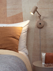 It’s about RoMi Wandleuchte Montreux in Sand mit verstellbarem Arm an einer Wand mit gestreifter Tapete, neben dem Bett.