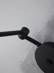 Detailansicht der RoMi Wandleuchte Montreux in Schwarz: schwarzer Metallarm mit Gelenk und rundem Wandmontage-Element vor heller Wand.