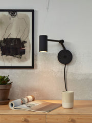 RoMi Wandleuchte Montreux in Schwarz: schwarze Wandleuchte mit zylindrischem Schirm und Gelenkarm an heller Wand.