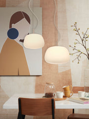 Zwei weiße Glas-Hängeleuchten "It's about RoMi Sapporo" mit Kabel hängen über einem weiß-beigen Esstisch mit Stühlen.