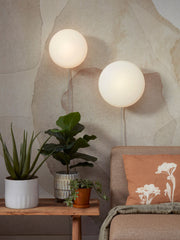 Zwei runde weiße Glas-Wandleuchten leuchten warm über einem Sofa an einer beigen Wand.