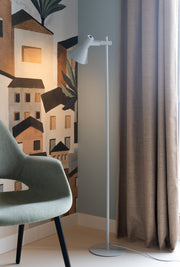 It’s about RoMi Stehleuchte Stavanger in Hellgrau neben einem Sessel und einer Wand mit Stadtillustration.