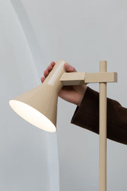 It’s about RoMi Stehleuchte Stavanger in Beige: Eine Hand hält den runden Eisenschirm, der Leuchtenkopf ist seitlich geneigt.