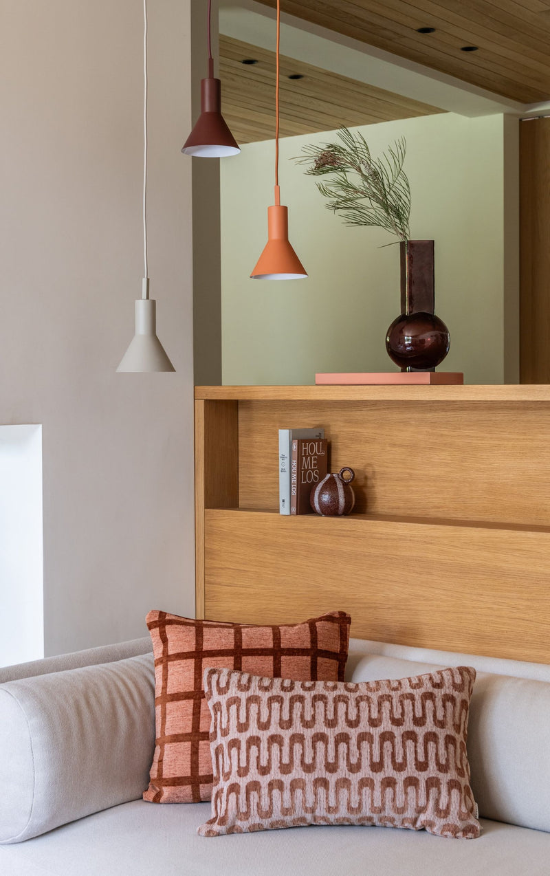 Hängeleuchten mit konischem Metallschirm in Terrakotta, Orange und hellem Grau über einem Sofa.