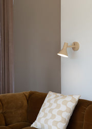 Die RoMi Wandleuchte Stavanger in Beige mit schwenkbarem Schirm hängt an einer Wand neben einem braunen Samtsofa.