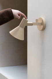 It’s about RoMi Wandleuchte Stavanger in Beige: Eine Hand betätigt den Schalter am schwenkbaren Schirm der Eisen-Wandleuchte.