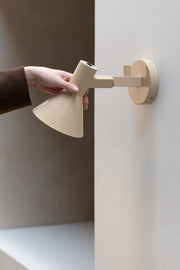 It's about RoMi Wandleuchte Stavanger in Beige: Eine Hand schwenkt den beigen Metallschirm an einem Wandarm aus der Wand.