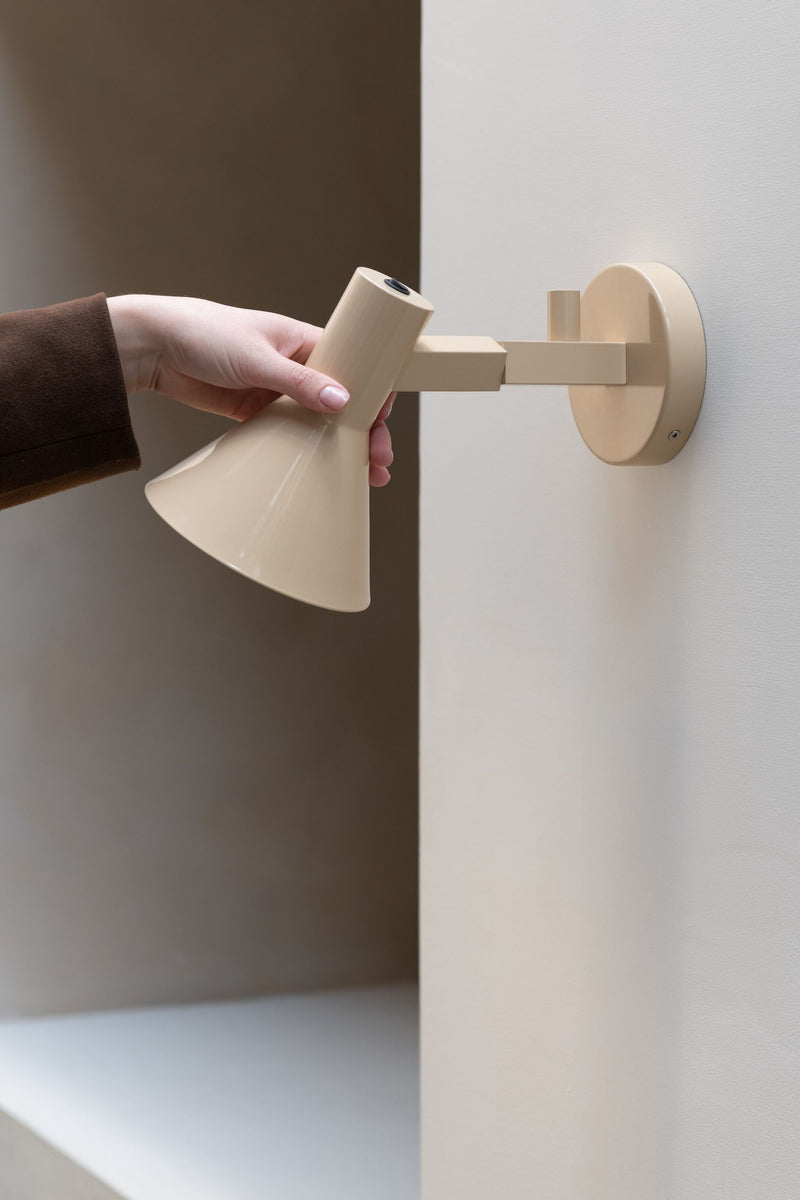 It's about RoMi Wandleuchte Stavanger in Beige: Eine Hand schwenkt den beigen Metallschirm an einem Wandarm aus der Wand.