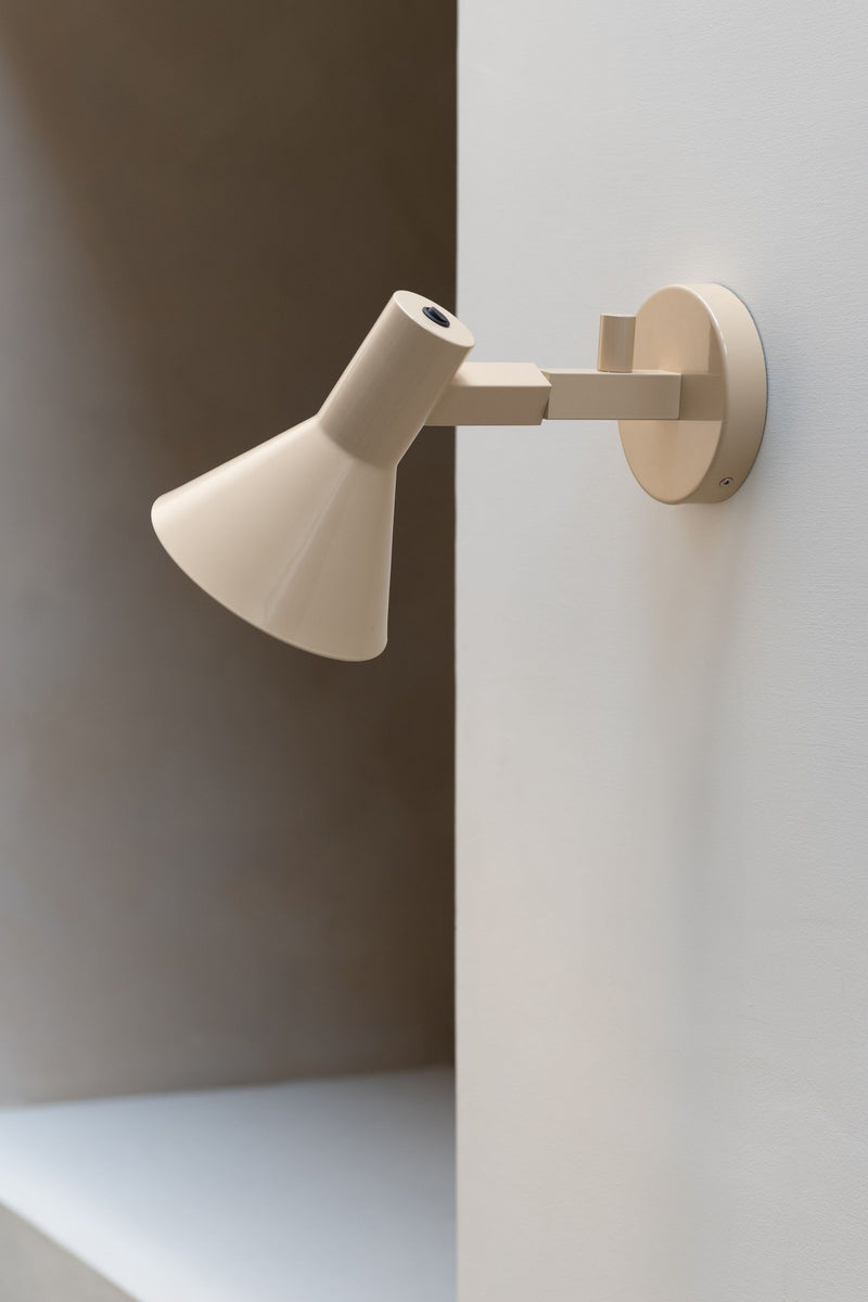 It’s about RoMi Wandleuchte Stavanger in Beige: beige Wandleuchte mit konischem Schirm und schwenkbarem Arm vor heller Wand.