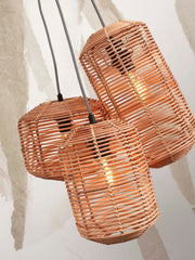 Dreiarmige Hängeleuchte Tanami von Good&Mojo mit Lampenschirmen aus naturfarbenem Rattan, eingeschaltet, vor heller Wand.