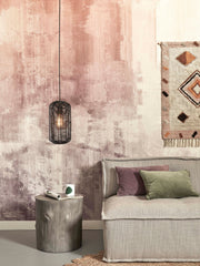 Schwarze Hängeleuchte Tanami aus Rattan mit Eisengestell über einem grauen Sofa in einem Wohnzimmer mit rosafarbener Wand.