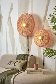 Good&Mojo Wandleuchte Tanami aus Rattan in Natur: zwei runde Schirme mit Lichtquelle, an einer hellen Wand über einem Sofa.