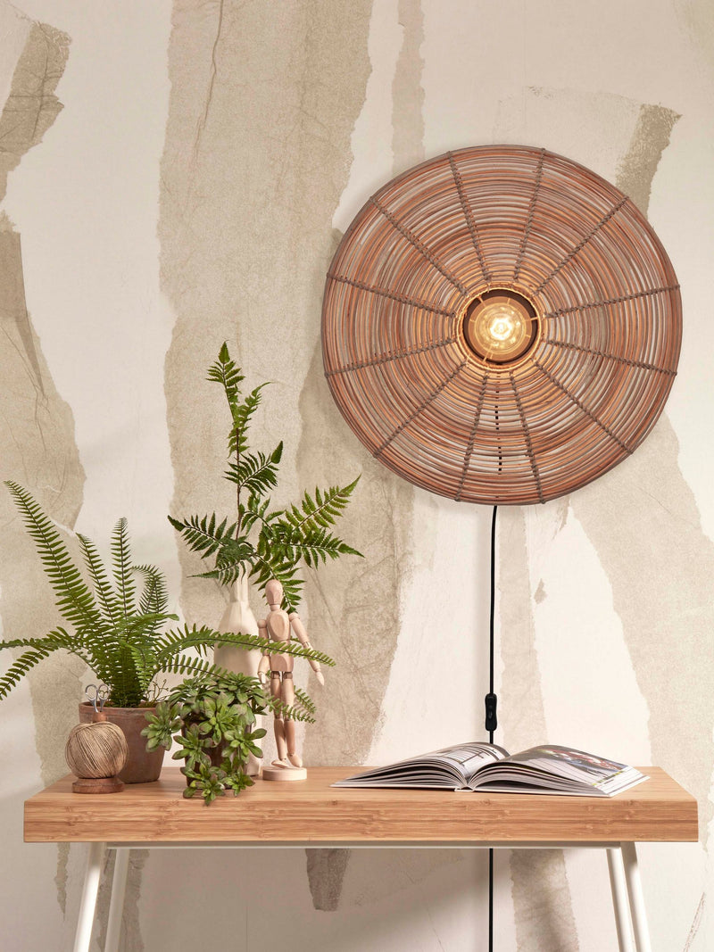 Good&Mojo Wandleuchte Tanami aus Rattan und Eisen in Natur mit rundem Rattanschirm, eingeschaltet über einem Holztisch.