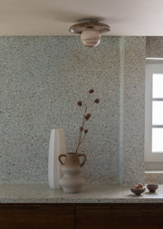 Deckenleuchte Tivoli von It's about RoMi mit Marmor-Scheibe vor einer Terrazzo-Wand, daneben eine helle Vase.