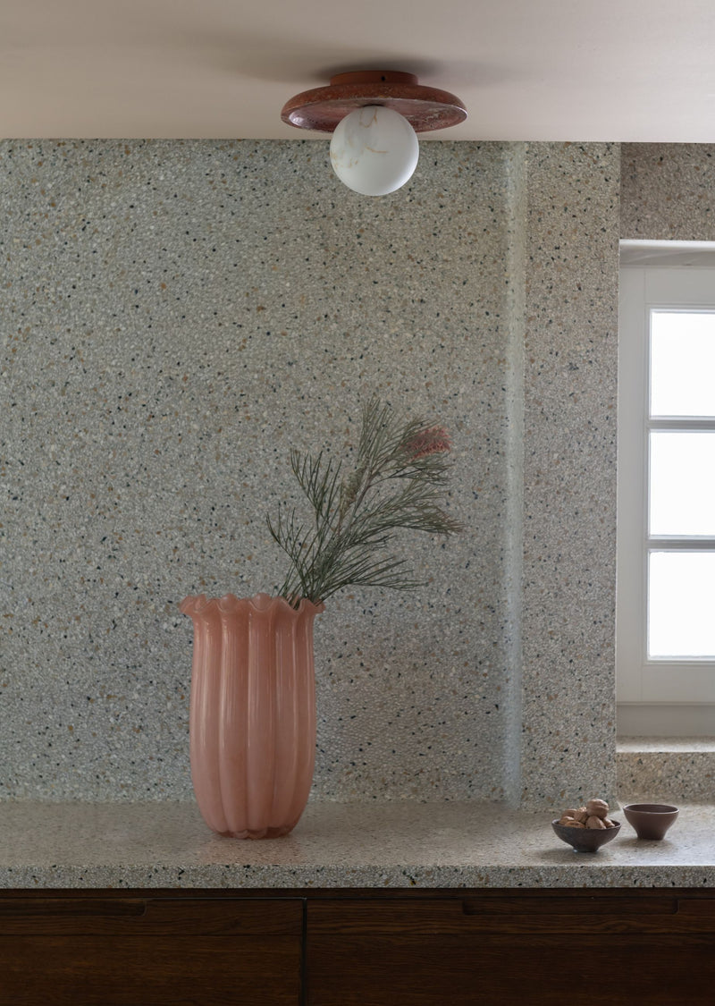 Deckenleuchte Tivoli in Terrakotta mit Marmor-Scheibe und Glasschirm über einer Terrazzo-Wand mit rosafarbener Vase.