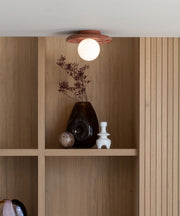 Deckenleuchte Tivoli in Terrakotta mit weißer Glaskugel, darüber Trockenblumen und Vasen in einem Holzregal.
