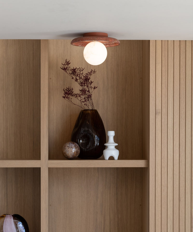 Deckenleuchte Tivoli in Terrakotta mit weißer Glaskugel, darüber Trockenblumen und Vasen in einem Holzregal.