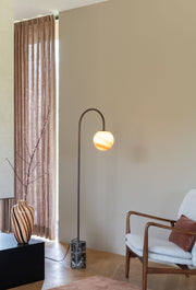 Stehleuchte RoMi Tivoli mit gebogenem Metallarm, bernsteinfarbenem Glasschirm und rundem Marmorfuß im Wohnraum.