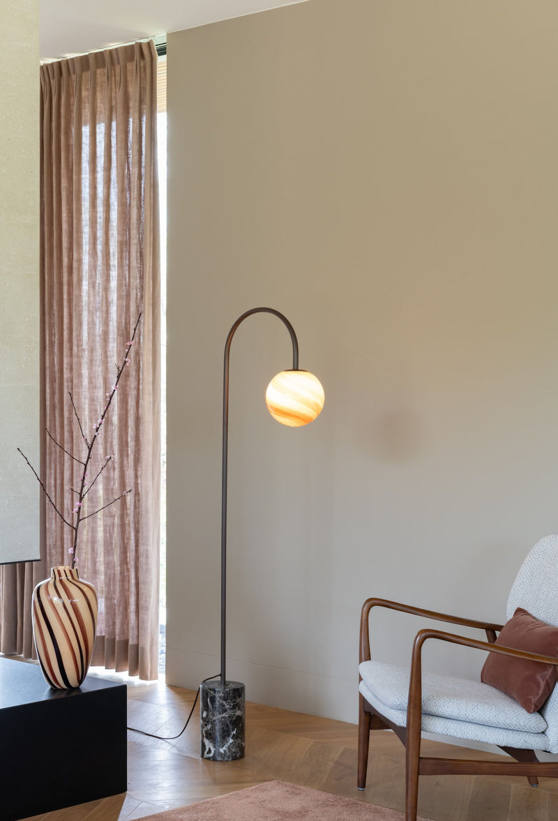 Stehleuchte RoMi Tivoli mit gebogenem Metallarm, bernsteinfarbenem Glasschirm und rundem Marmorfuß im Wohnraum.