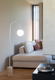 Stehleuchte It's about RoMi Tivoli in Weiß mit rundem Glasschirm und Travertinfuß, neben einem beigen Sofa im Wohnraum.