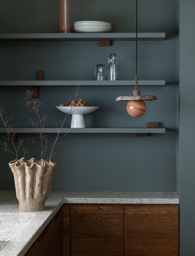 Hängeleuchte It's about RoMi Tivoli aus Marmor in Braun, über Regalen mit Keramikschale und Vase vor dunkelgrüner Wand.
