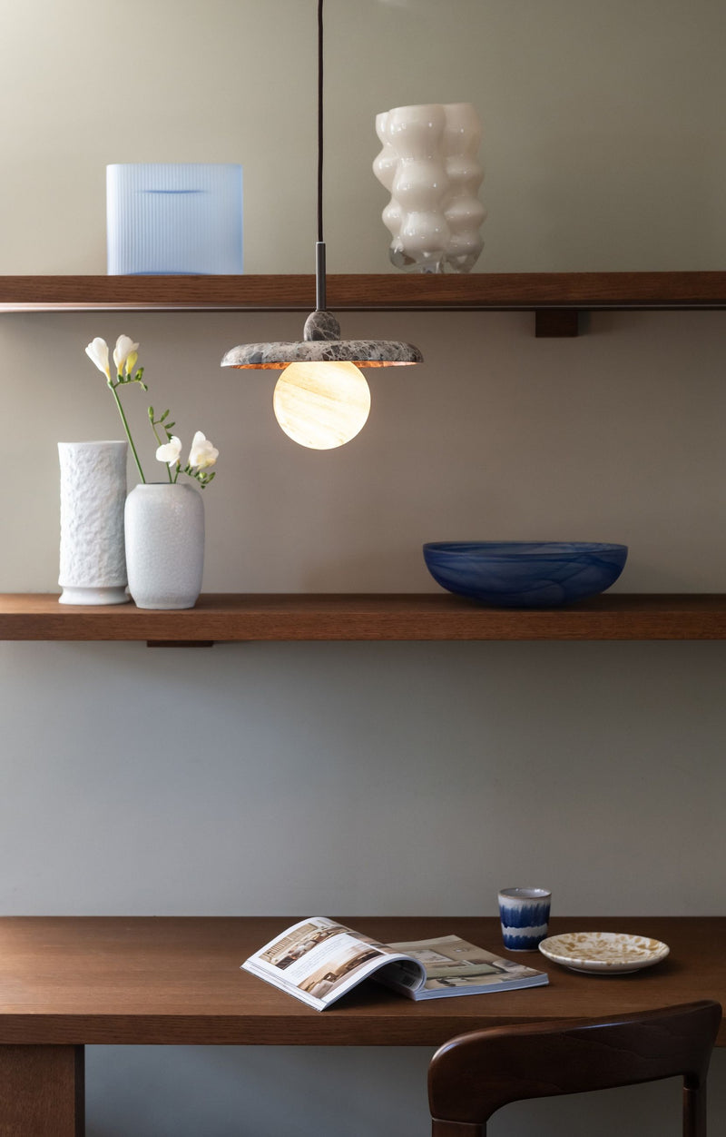 It’s about RoMi Hängeleuchte Tivoli aus Marmor in Braun, mit leuchtender Glaskugel über einem Holzregal mit Vasen und Schale.