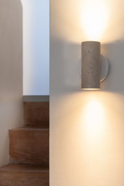Wandleuchte RoMi Tivoli in Weiß: zylindrischer Travertin-Schirm mit rundem weißem Eisengestell, warm an der Wand strahlend.