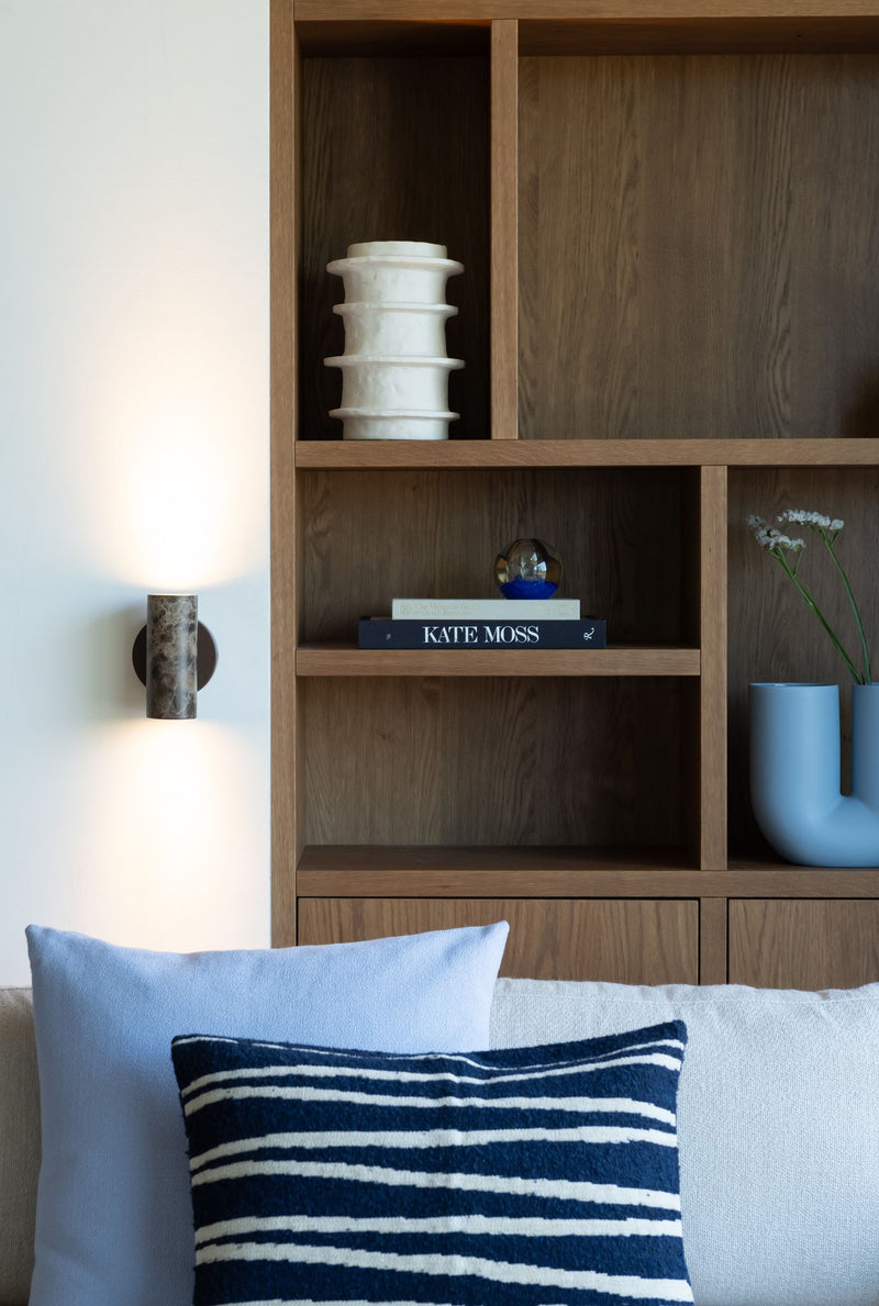 Braune Marmor-Wandleuchte It's about RoMi Tivoli neben einem Holzregal mit weißer Keramikvase, Büchern und Kissen.