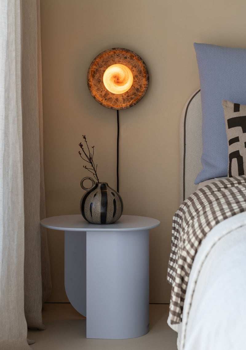 Runde braune Marmor-Wandleuchte "It's about RoMi Tivoli", eingeschaltet über einem Nachttisch mit blauer Vase.