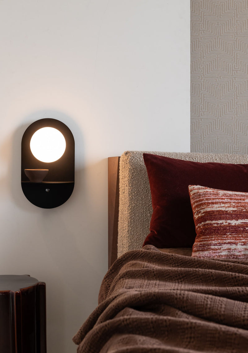 It's about RoMi Wandleuchte Tokyo: schwarze ovale Wandleuchte mit rundem Glasschirm und kleiner Ablage über einem Bett